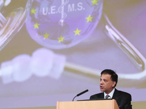 Chaand Nagpaul speaks at a podium in front of the EU flag