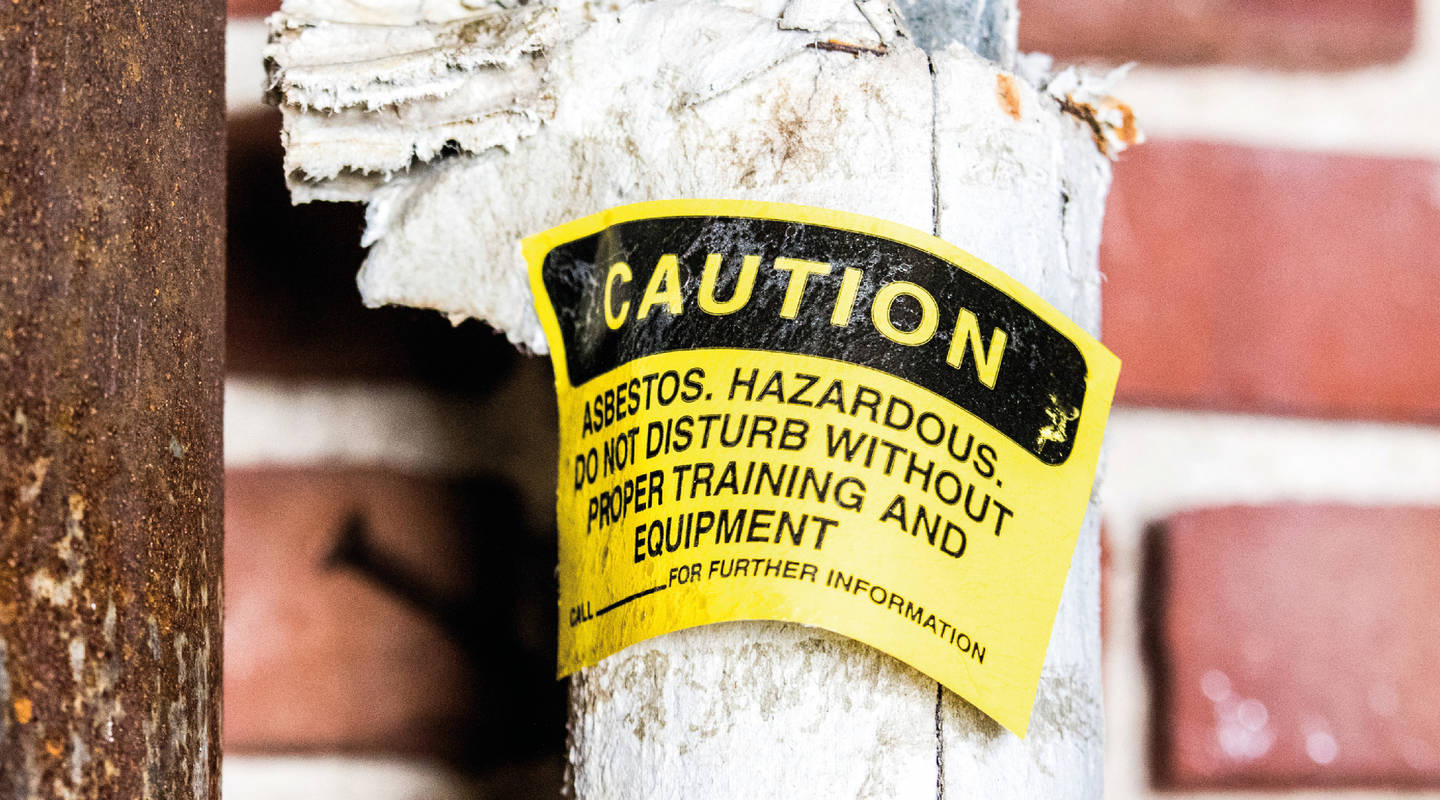 A hazard sign strapped to external asbestos post on a building