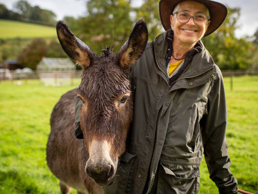 Debbie Cohen depicted with her arm around a donkey on her farm