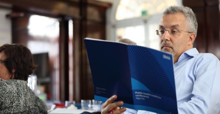 A man sat at a table in BMA House reading a BMA agenda on public health