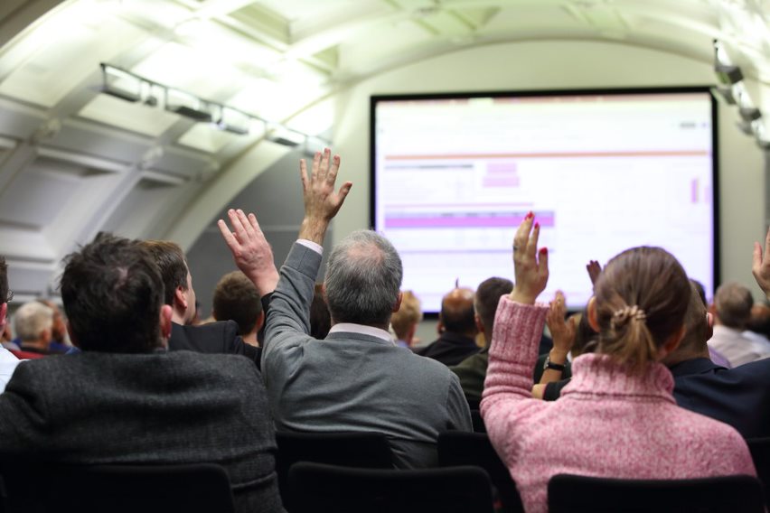 Members of staff at BMA house attending a meeting from behind. They are seated facing a presentation that is out of focus and some are raising their hands.
