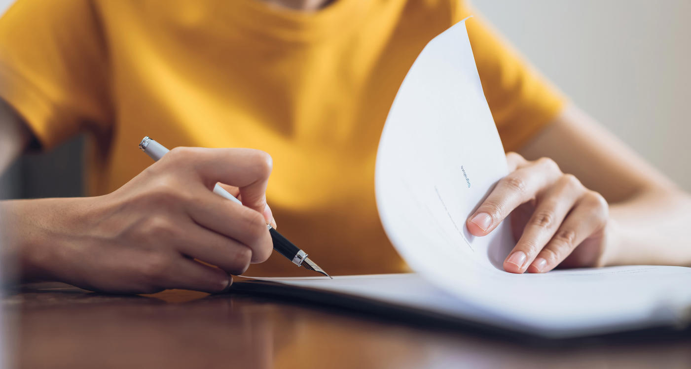 Detail of a woman in a bright yellow top writing in a document with a nice pen