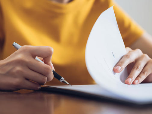 Detail of a woman in a bright yellow top writing in a document with a nice pen