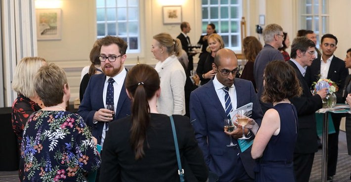 An event at BMA house. Men and women in semi-formal dress gather and talk with drinks in hand.