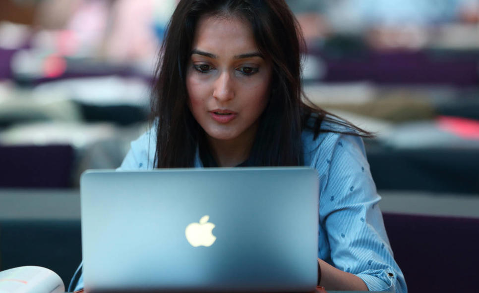 A woman sits over an open laptop, concentrating.