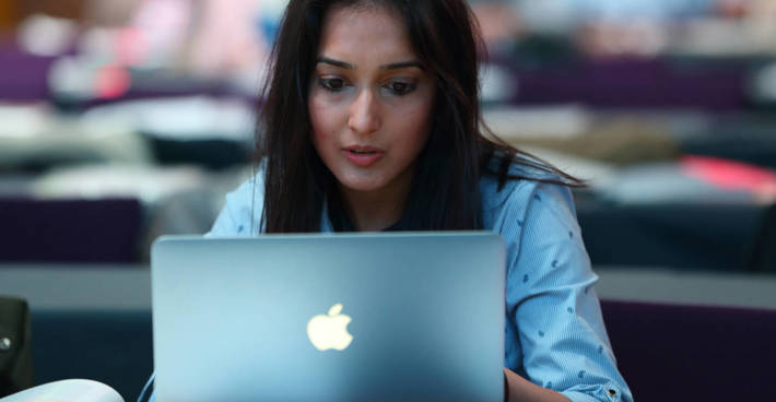 A woman sits over an open laptop, concentrating.