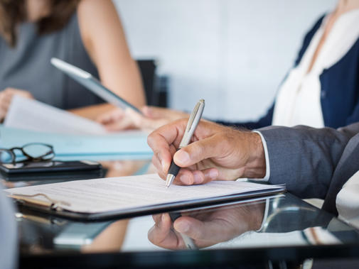 Detail of people in business attire sat at a meeting desk holding pens