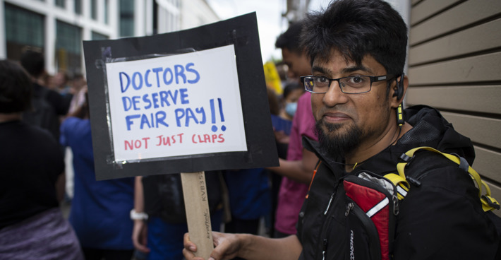 Protestor with sign saying 'Doctors deserve fair pay!'