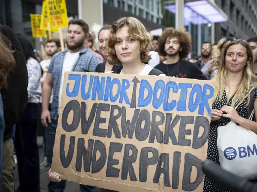 Protestor holding sign saying "junior doctor - overworked and underpaid"