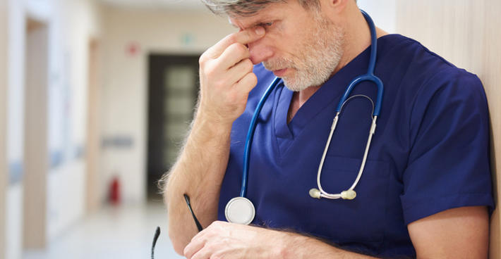 Tired Doctor In Scrubs Leaning In Corridor