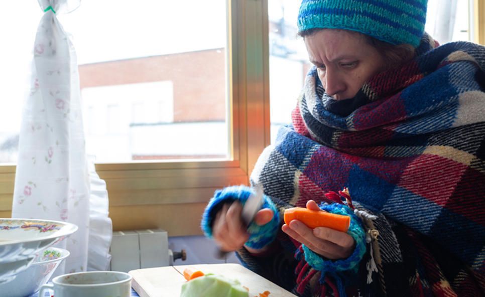 Woman Wrapped In Blanket, Gloves And Hat Preparing Vegetables In Kitchen