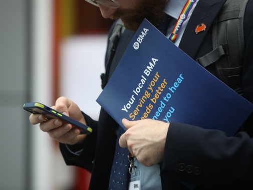 Man at ARM studies phone whilst holding a BMA benefits booklet in his other hand. He wears a BMA rainbow lanyard.